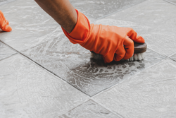 person wearing orange gloves and scrubbing tile