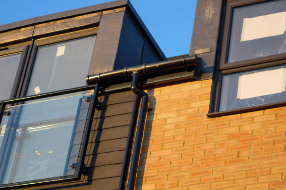 Modern building with windows, brick wall, and black rain gutter.