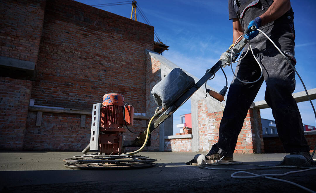 Worker cleaning and smoothing freshly poured concrete on a construction site.