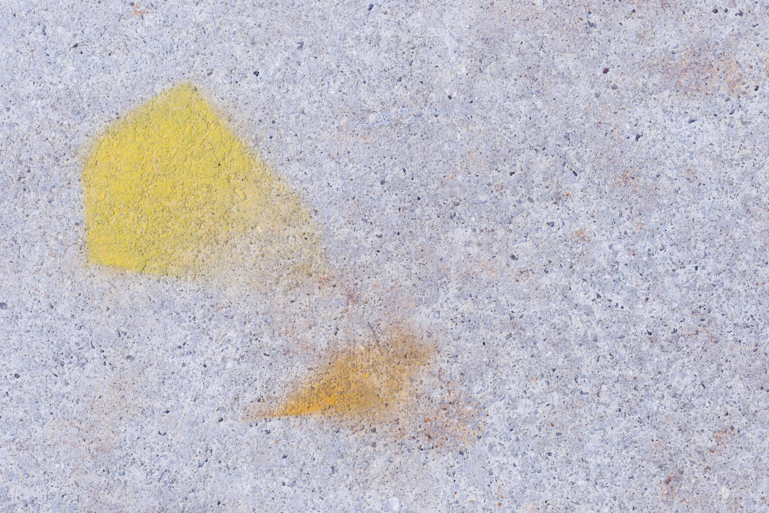 Faded yellow paint stain on concrete surface demonstrating how to remove paint from concrete.