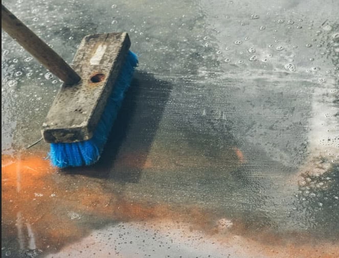Worker pressure washing a concrete surface with a concrete cleaning solution.
