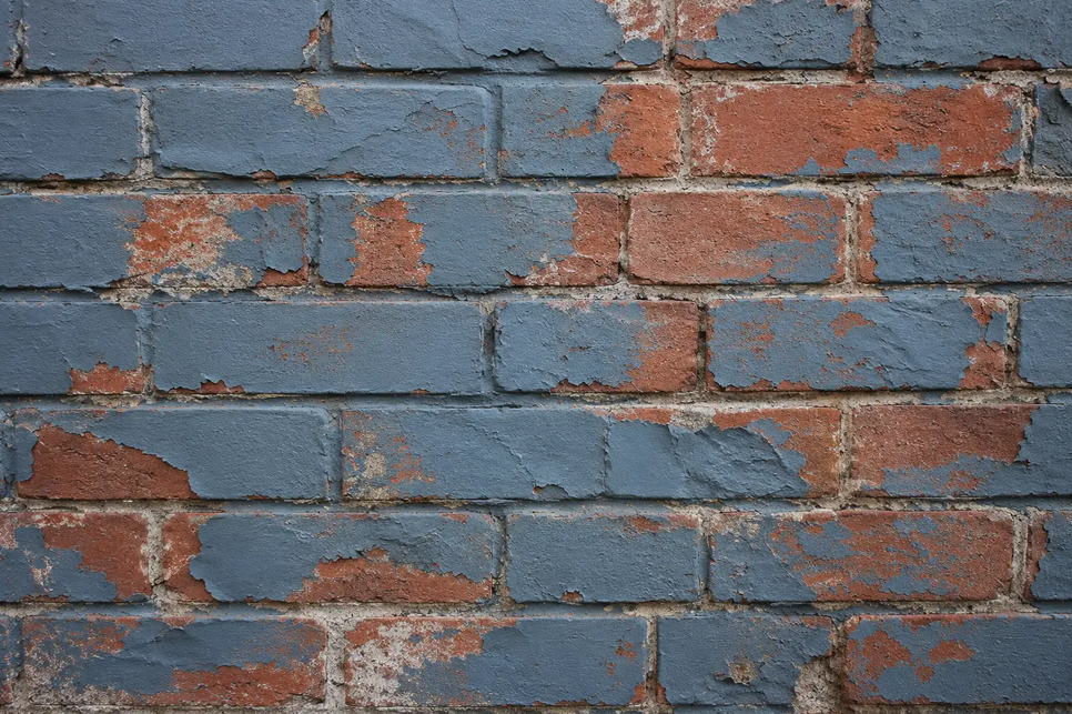Close-up of a painted brick wall with peeling paint exposing the original red brick beneath.